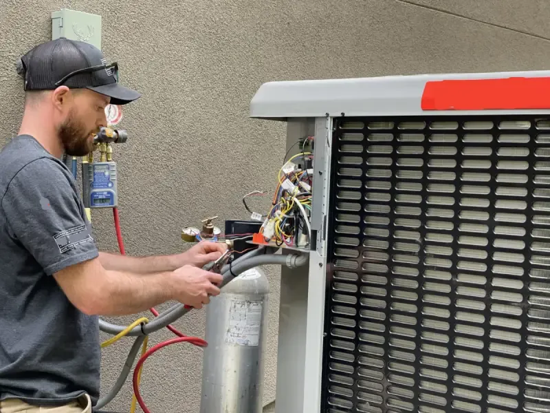 HVAC technician working on an outdoor condenser unit with tools and gauges.